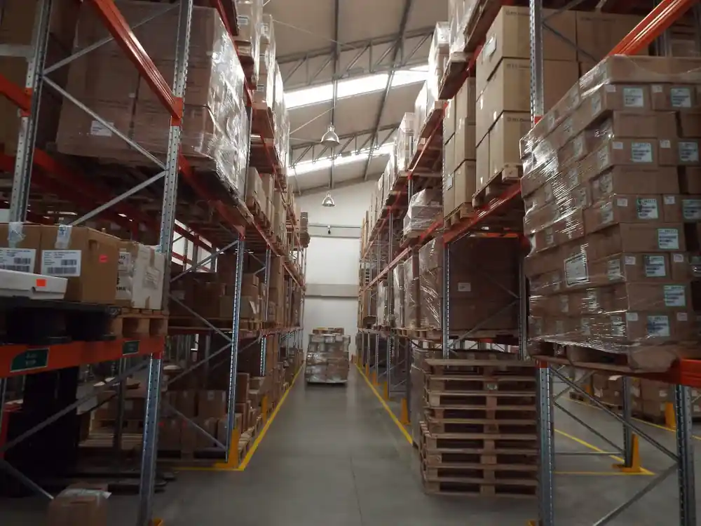 A narrow aisle between tall shelving bays stacked with cartons, pallets resting at floor level