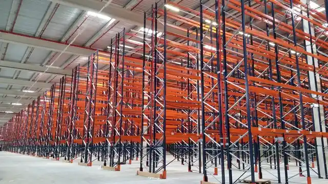 Rows of empty orange and blue racking beams receding into a large, bright hall