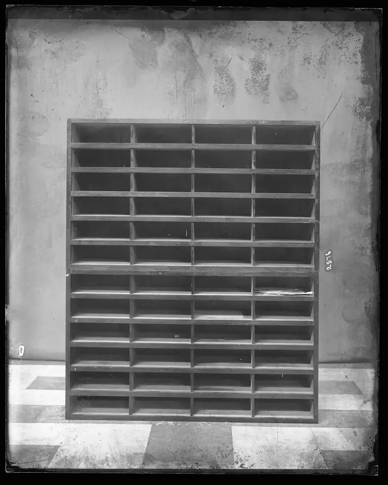 A black-and-white photograph of an empty wall of pigeonhole shelves, every slot the same size